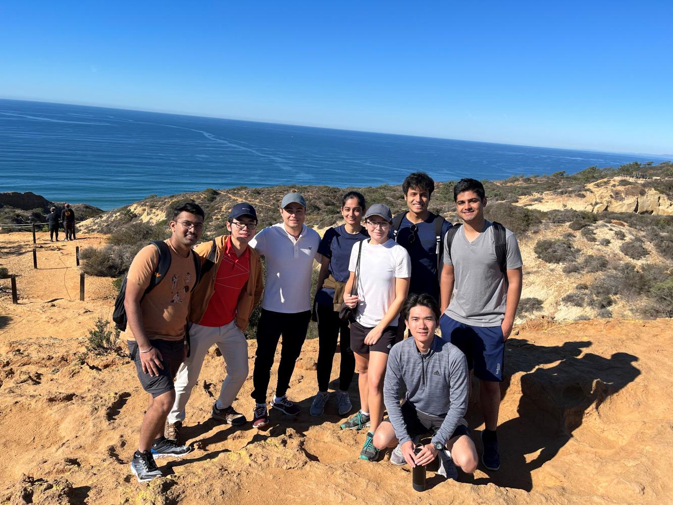 Picture of eight RoboGrads members at the Torrey Pines trail with the ocean in the background